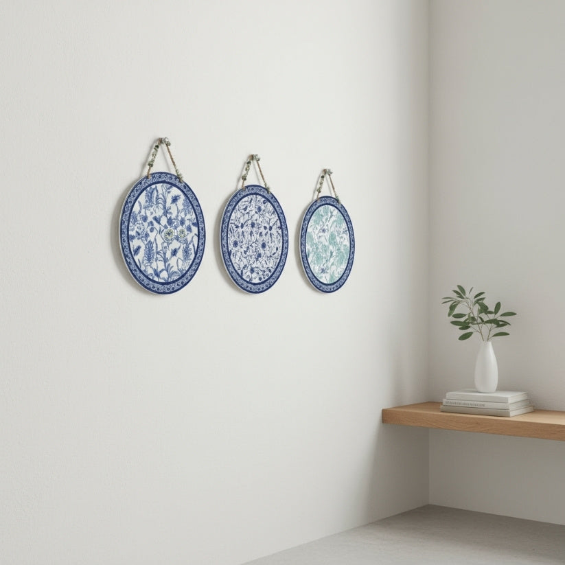Three decorative plates with blue and white patterns hanging on a white wall above a wooden shelf.