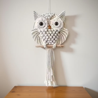 Macrame owl wall hanging on a wooden table against a plain wall