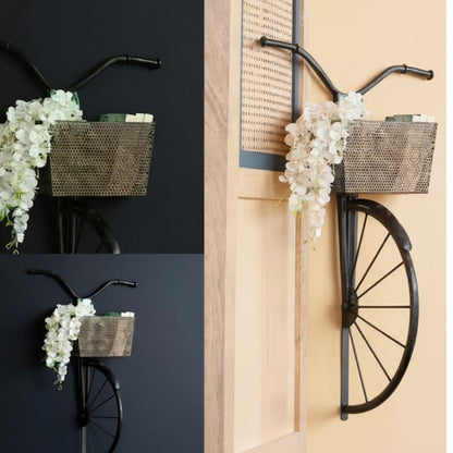 Decorative bicycle with basket and floral arrangement on a wall.